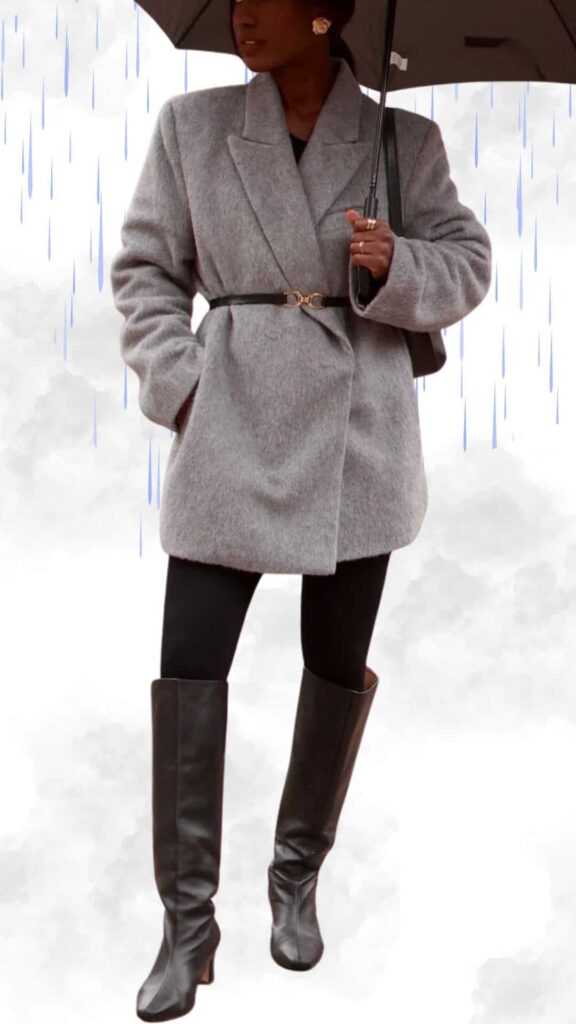 The outfit features a cozy gray wool blazer cinched with a black belt, paired with sleek black leggings for a streamlined look. Knee-high black leather boots add sophistication while ensuring practicality in rainy weather. An umbrella complements the ensemble, making it both chic and functional for fall and winter outings.