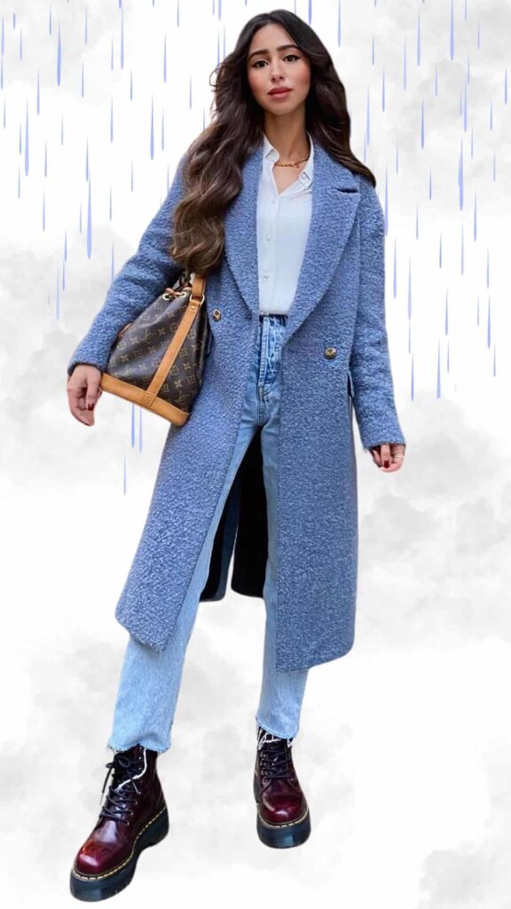 The outfit features a cozy, textured light blue overcoat with a structured silhouette, complemented by a classic white button-up shirt underneath. The look is paired with high-waisted light blue jeans and stylish burgundy platform boots, adding a touch of chic sophistication. A distinctive brown handbag completes the ensemble, making it ideal for staying warm and fashionable in rainy fall and winter weather.
