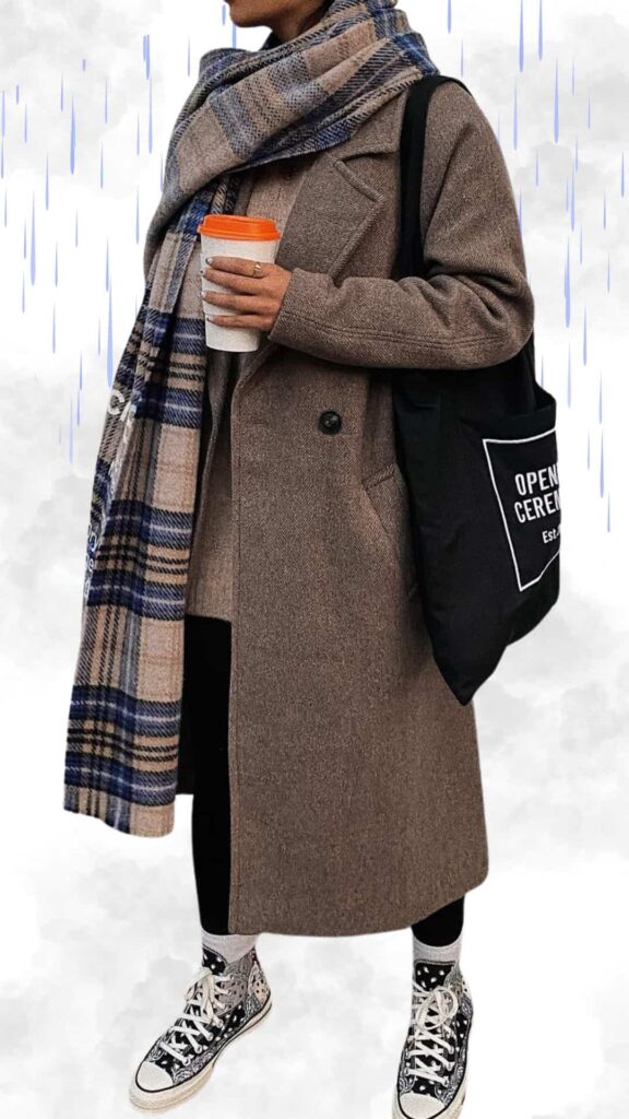 The outfit features a long, textured brown coat that offers warmth and elegance, paired with a cozy plaid scarf in beige, blue, and gray tones for added flair. Underneath, a neutral top is complemented by sleek black leggings, while stylish black and white patterned high-top sneakers provide a playful yet chic finish. A black tote bag completes the look, making it practical for rainy fall and winter days.