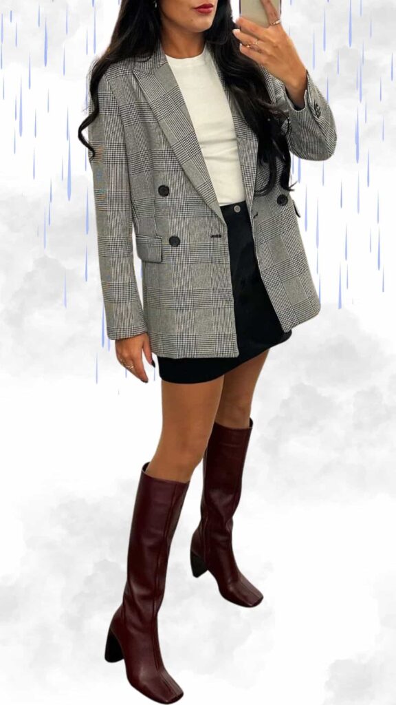 The outfit features a stylish, gray plaid double-breasted blazer layered over a fitted white top, paired with a sleek black mini skirt for a modern silhouette. Complete with knee-high, burgundy heeled boots, this look combines classic elegance with contemporary flair, perfect for rainy fall or winter days. The textures and bold colors ensure a chic appearance while providing warmth and comfort.