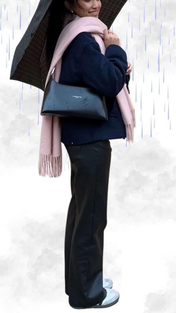 The outfit features a chic navy coat paired with sleek black trousers, both made from water-resistant materials for rainy weather. A soft blush scarf adds warmth and texture, while stylish gray ankle boots complete the look, ensuring comfort and sophistication. A shiny black handbag provides a polished accent, making this ensemble perfect for staying warm and dry while looking effortlessly elegant.