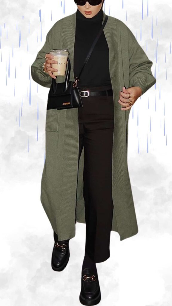 The outfit features a long, olive green knit cardigan over a fitted black turtleneck, paired with tailored dark trousers. Stylish black loafers with gold accents provide elegance, while a small black handbag adds a chic touch. The combination offers a warm, sophisticated look ideal for rainy fall and winter days.
