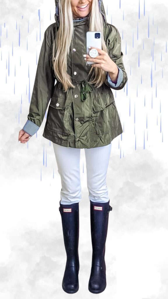 The outfit features a stylish olive green raincoat with a cinched waist and snap closures, layered over a classic striped long-sleeve shirt peeking from the sleeves. The look is paired with slim white pants and tall navy rubber boots, ensuring both warmth and a chic appearance during rainy fall and winter weather. This ensemble is practical yet fashionable, perfect for staying dry while making a statement.