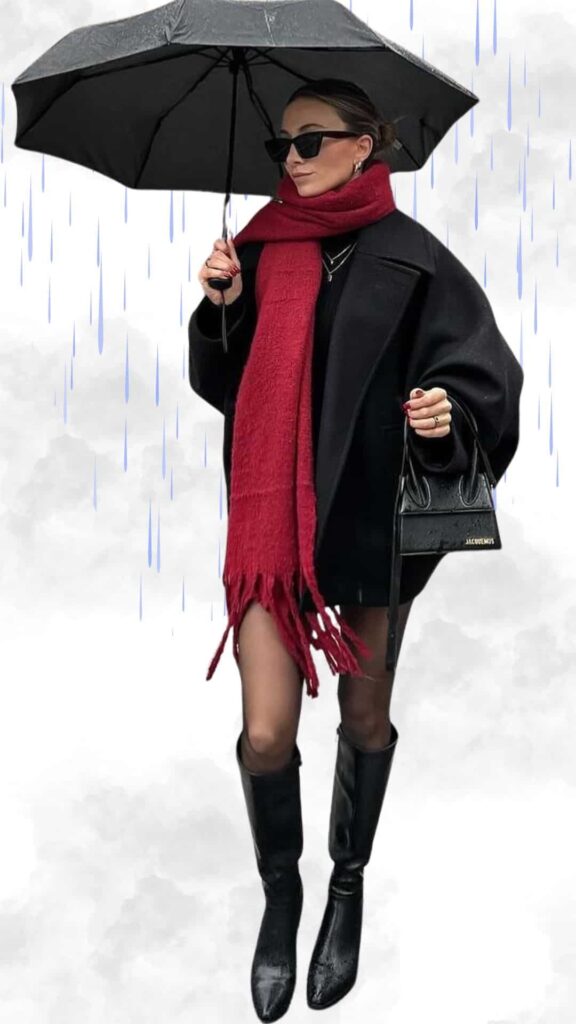 The outfit features an oversized black coat layered over a fitted black sweater dress, paired with sleek black knee-high heeled boots. A vibrant red scarf adds a pop of color, while the model holds a black umbrella to shield against the rain, completing the chic look with oversized sunglasses and a small black handbag. The textures include smooth fabric for the coat and boots contrasted with the cozy warmth of the scarf, perfect for staying stylish and comfortable in wet, cold weather.