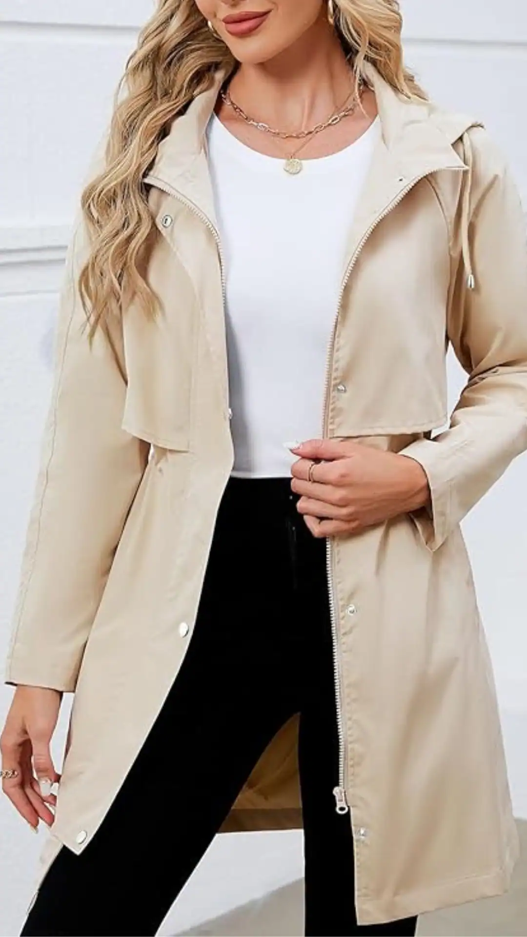 This rainy summer outfit features a light, beige waterproof jacket made of smooth, glossy fabric, paired with a classic white t-shirt and form-fitting black pants. The overall vibe is modern and practical, perfect for casual outings in unpredictable weather.