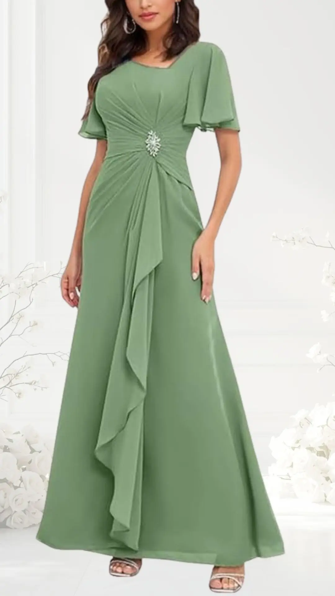 Sage green wedding guest dress featuring short flutter sleeves and a fitted bodice that gathers at the waist, accented by a delicate rhinestone embellishment. The flowing skirt drapes elegantly, creating a timeless and sophisticated silhouette suitable for formal occasions.