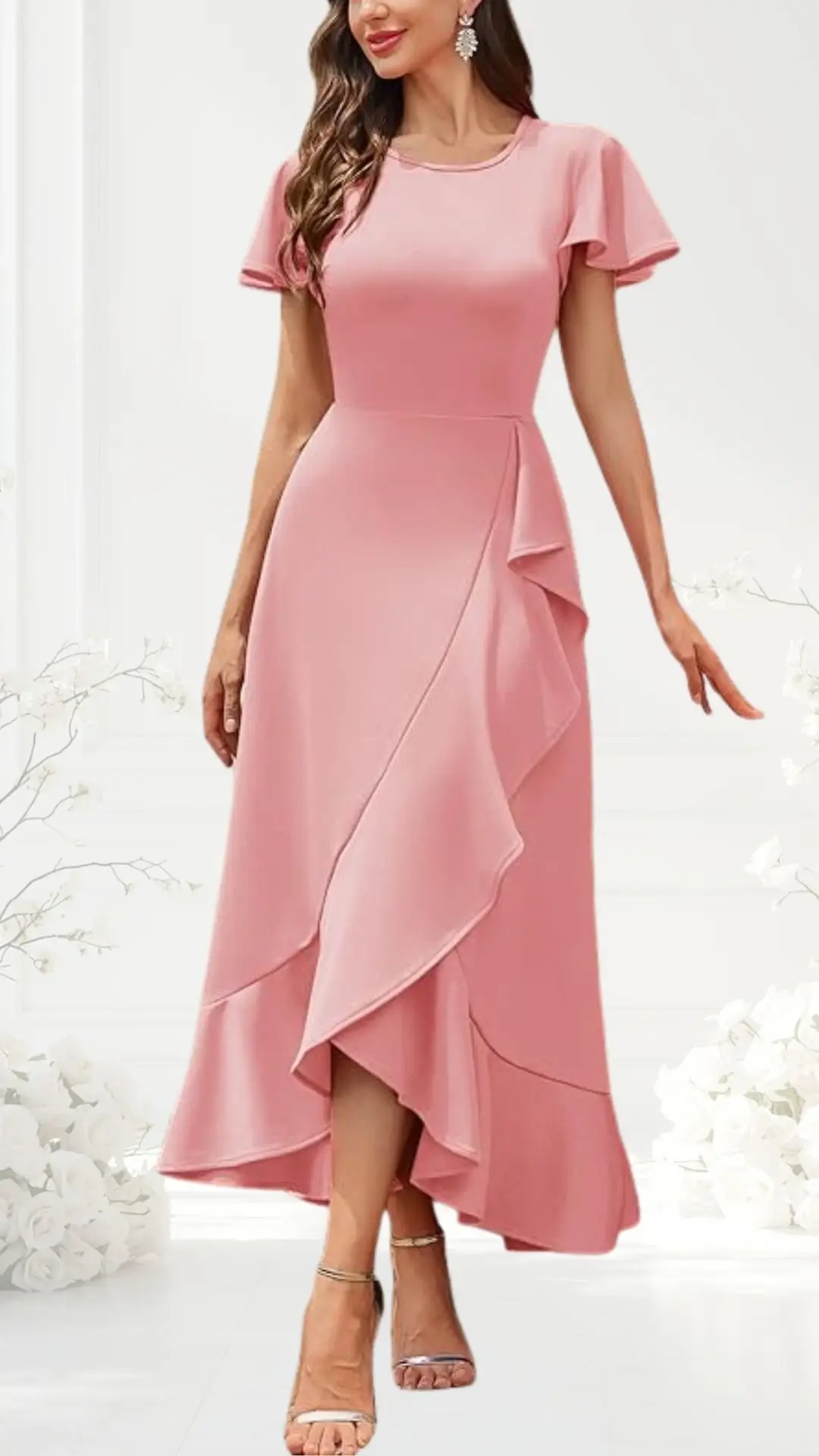 The dress features a soft pink hue with a fitted bodice and short flutter sleeves, creating a feminine silhouette. The skirt is designed with a cascading ruffle detail that flows from the waist to the knee, adding elegance and movement, while the hem is asymmetrical, offering a modern touch. Paired with strappy silver heels, this semi-formal dress is perfect for a wedding guest.