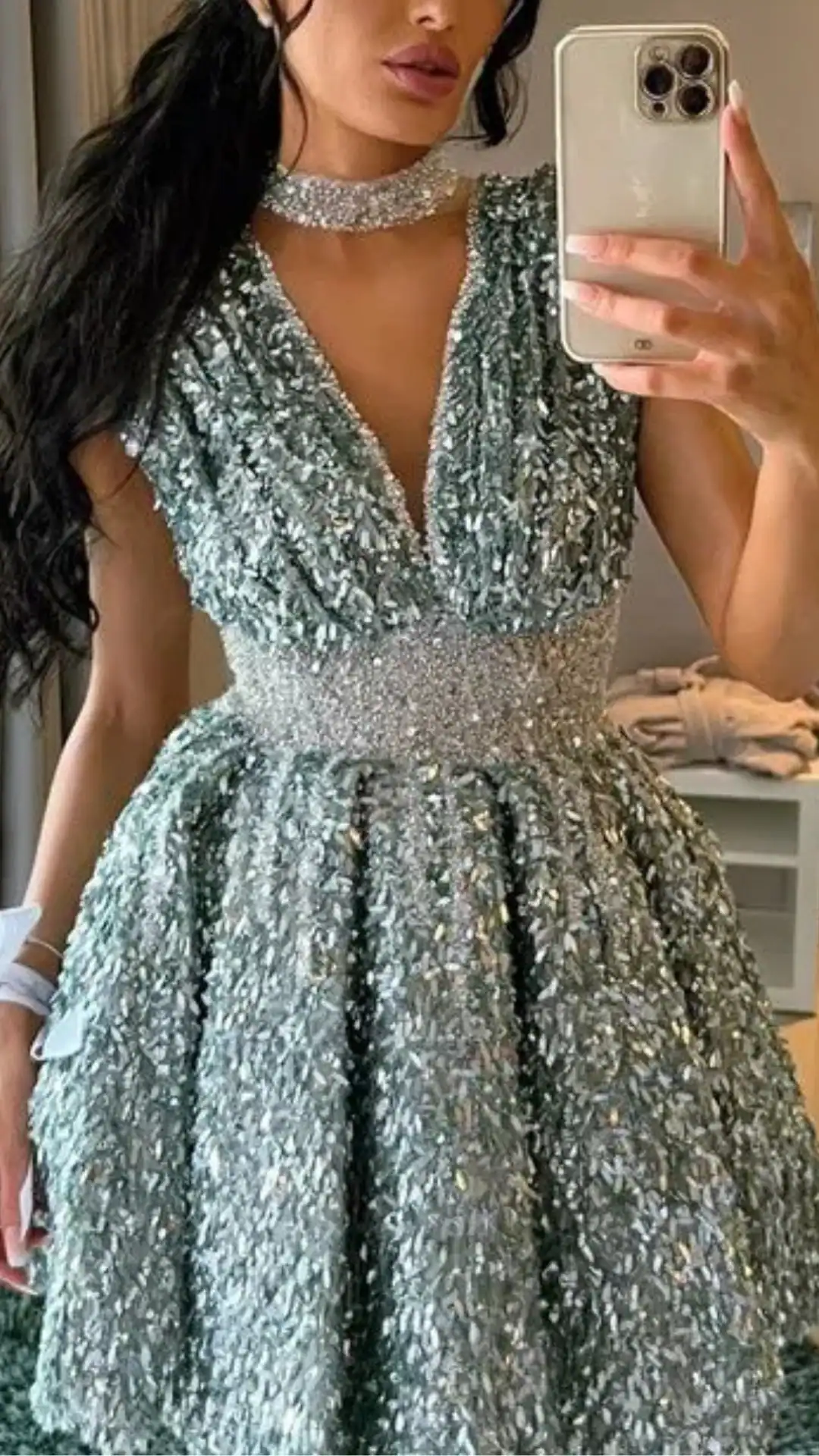 This shimmering sage green homecoming dress features a deep V-neckline and a voluminous skirt adorned with textured, sequined fabric that catches the light beautifully, creating an ethereal vibe. Designed for teenage girls, it is perfect for formal events like homecoming, combining a youthful elegance with a bold, statement-making style.