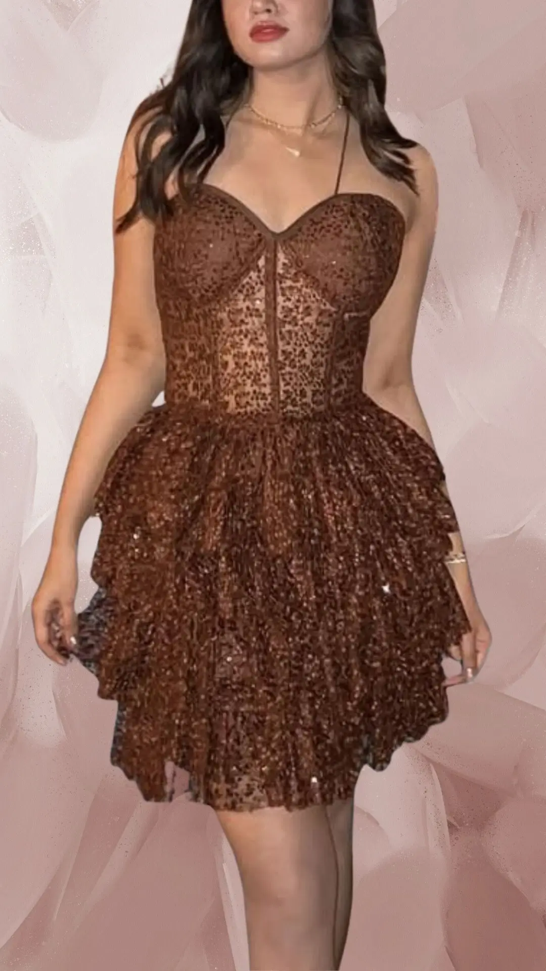 The outfit features a short, strapless brown dress adorned with intricate lace detailing and shimmering sequins, creating a textured, eye-catching effect. Its fitted bodice flows into a playful, tiered skirt that adds volume and movement, while a soft, elegant neckline accentuates the shoulders. Paired with matching shoes, this ensemble exemplifies a chic, glamorous style ideal for special occasions.