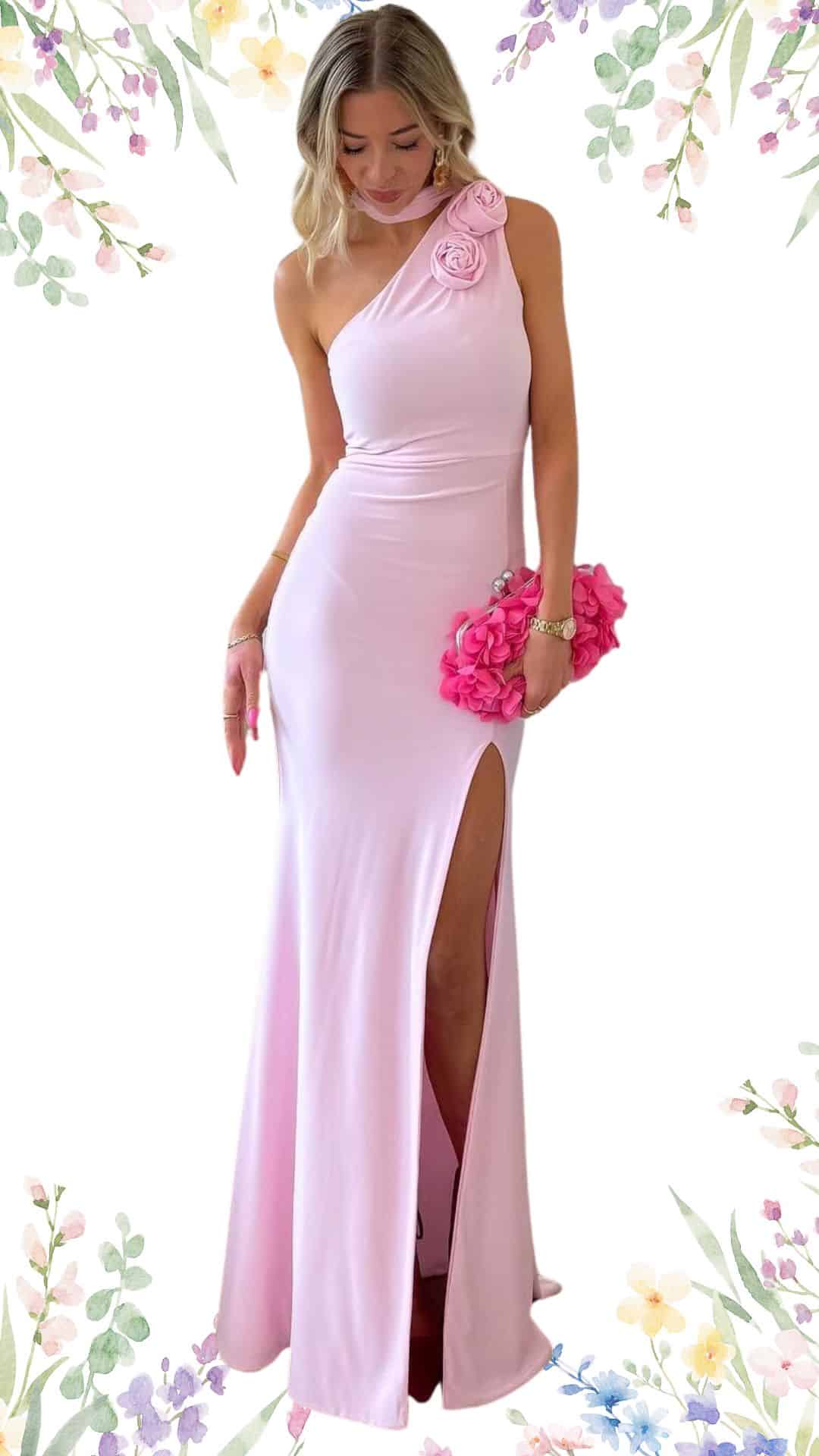 A long, elegant one-shoulder dress in a soft blush pink, featuring a fitted bodice that smoothly transitions to a flowing skirt with a high side slit. The neckline is subtly draped, accompanied by floral accents, while the fabric has a sleek, comfortable texture perfect for a spring wedding. The hemline gracefully sweeps the floor, adding sophistication to the overall design.