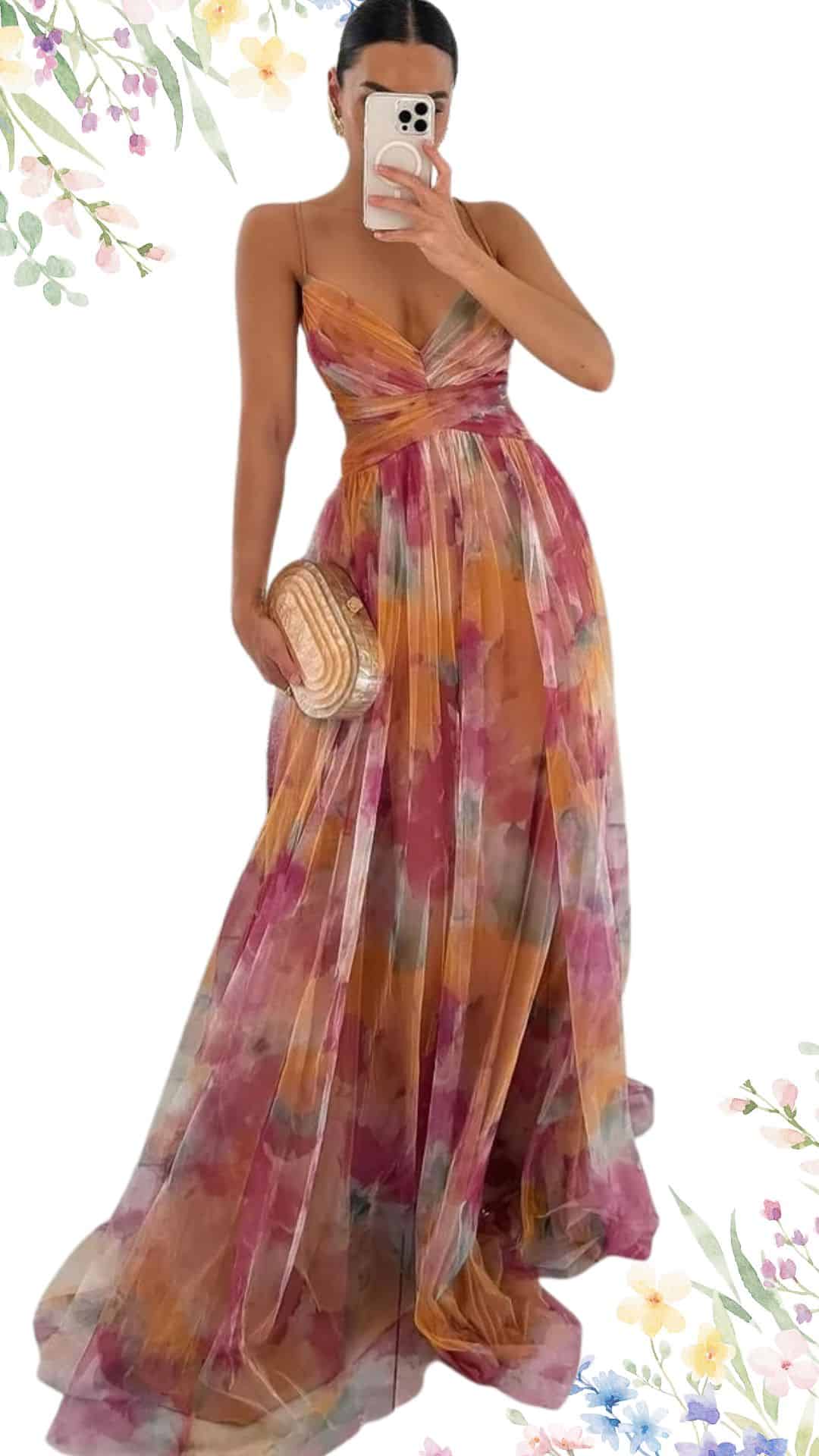 The dress features a flowing, floor-length silhouette in a soft, floral print with delicate shades of pink, orange, and light blue. It has a flattering V-neckline and thin spaghetti straps that lend an elegant touch, while the gently pleated fabric adds texture and movement, perfect for a spring wedding. The high-low hemline creates a graceful drape, enhancing its romantic appeal.