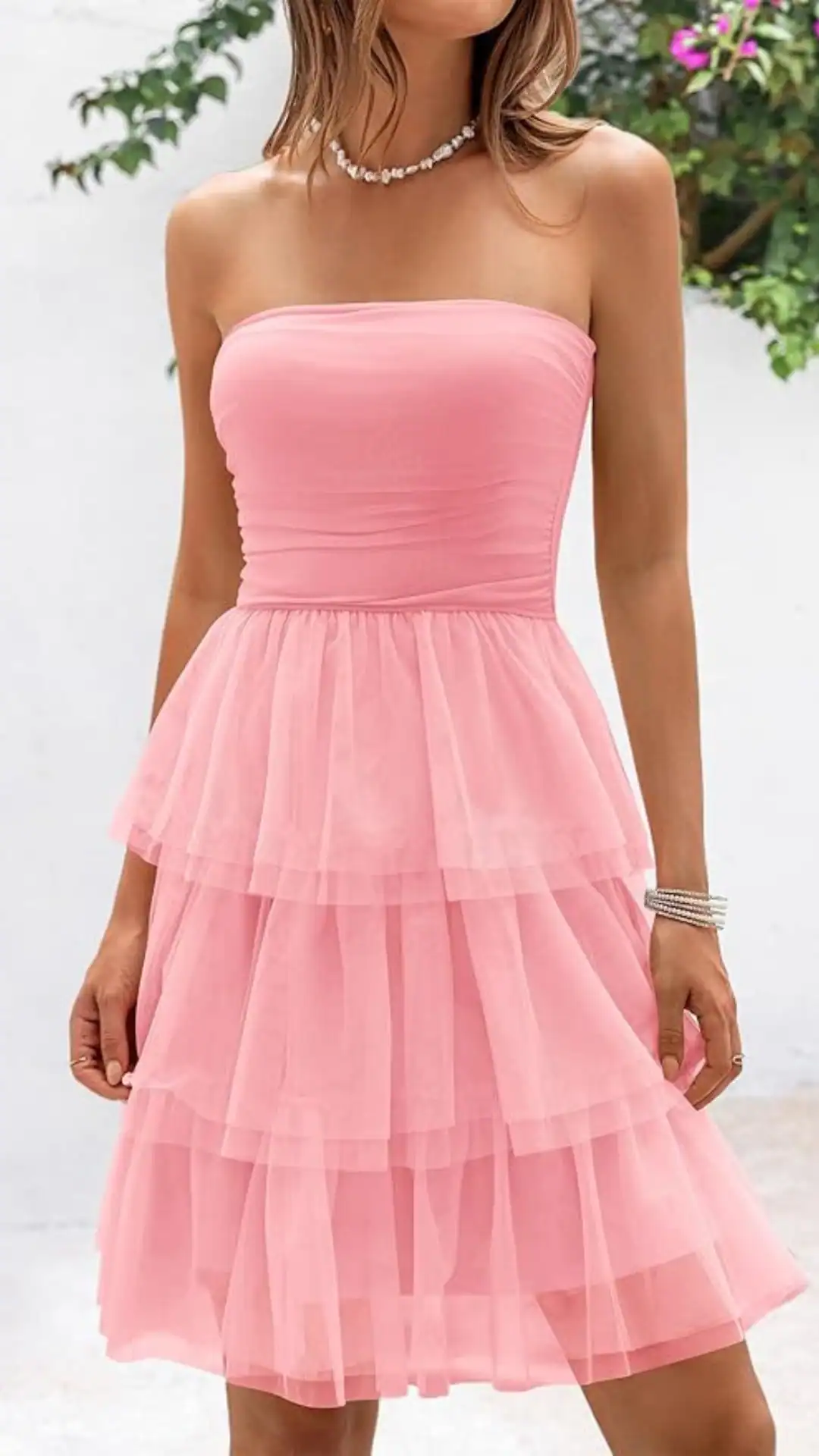 This strapless homecoming dress features a soft, sheer pink fabric with a layered tulle skirt, creating a playful and whimsical vibe. The fitted bodice accentuates the waist while allowing for a flowing, voluminous silhouette, making it ideal for formal events or school dances for teens.