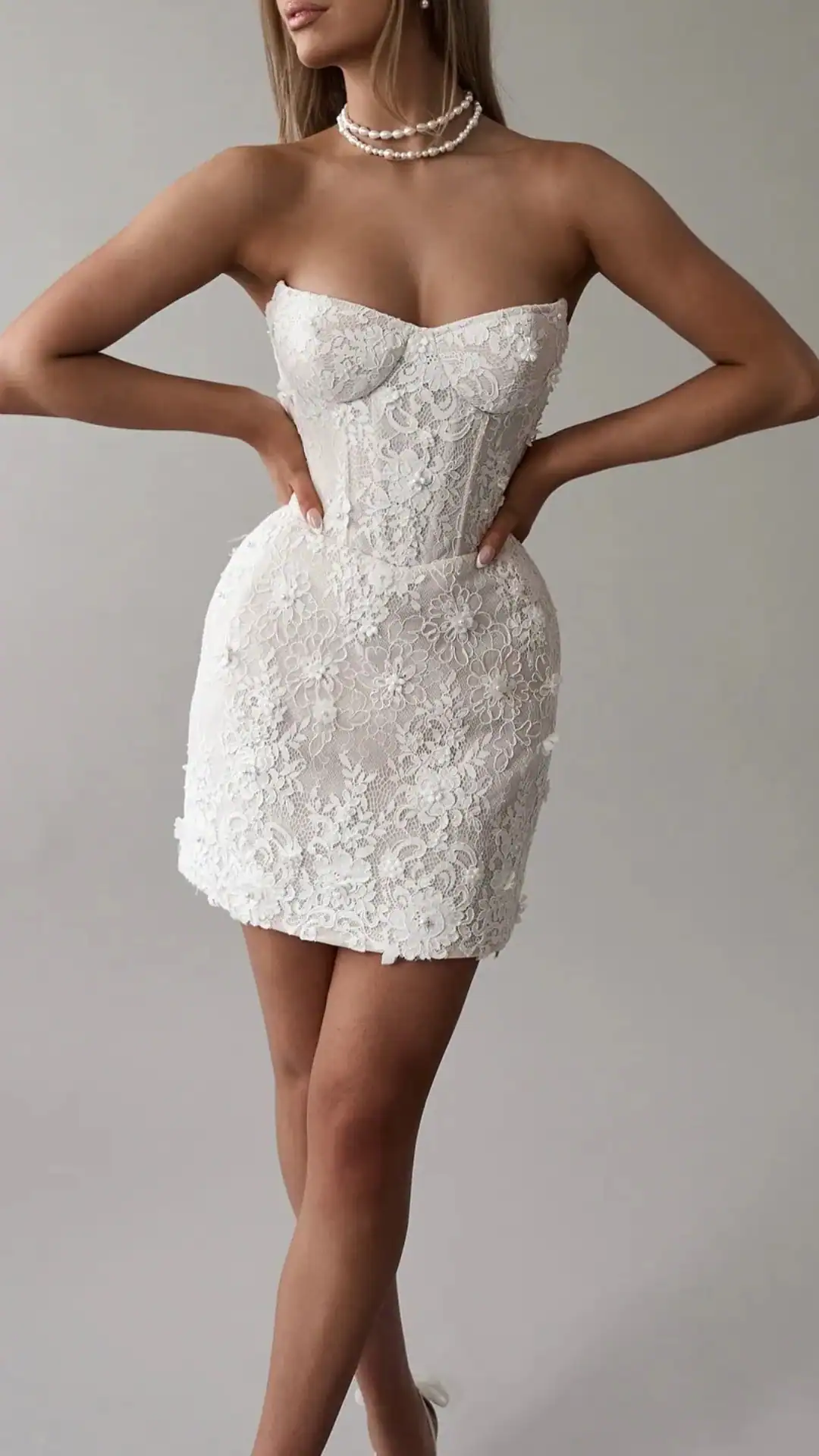 This stunning white homecoming dress features a fitted, corseted bodice adorned with intricate floral lace, offering a romantic and ethereal vibe. The sleek mini silhouette hugs the body and showcases delicate textures, making it a perfect choice for a formal event or school dance, ideal for teenage girls looking to make a stylish statement.
