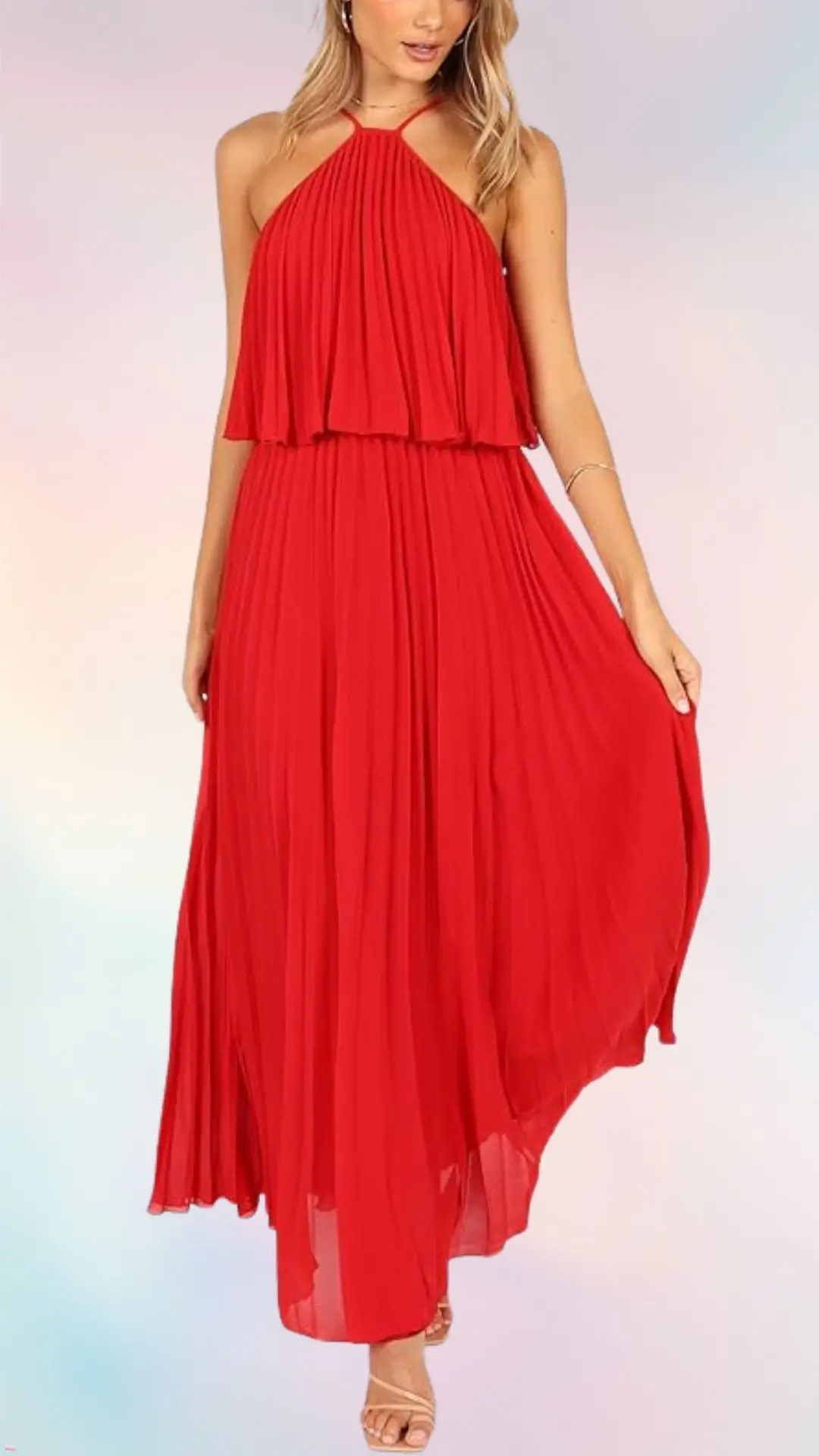 A flowy, red summer wedding guest dress with a halter neckline and layered bodice drapes elegantly to the floor. The lightweight fabric features intricate pleats, enhancing its movement, and the model is paired with minimalistic strappy sandals. The soft background complements the dress, emphasizing its bold color.