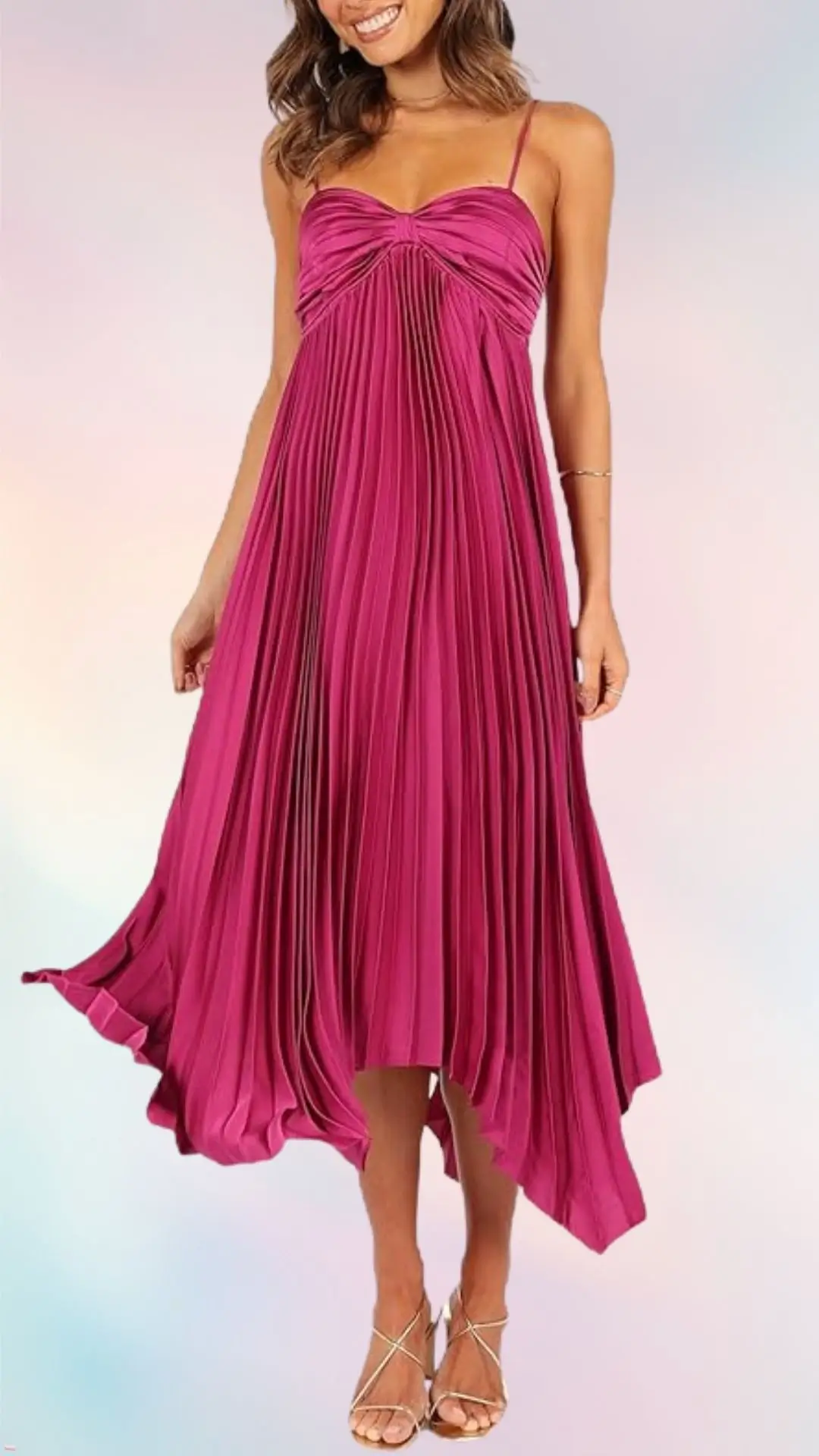 A woman stands in a flowing, knee-length dress featuring deep pink fabric with delicate pleats. The dress has thin, adjustable straps and a sweetheart neckline, creating a soft, elegant silhouette. She pairs the dress with strappy gold sandals, emphasizing a fresh, summery look.