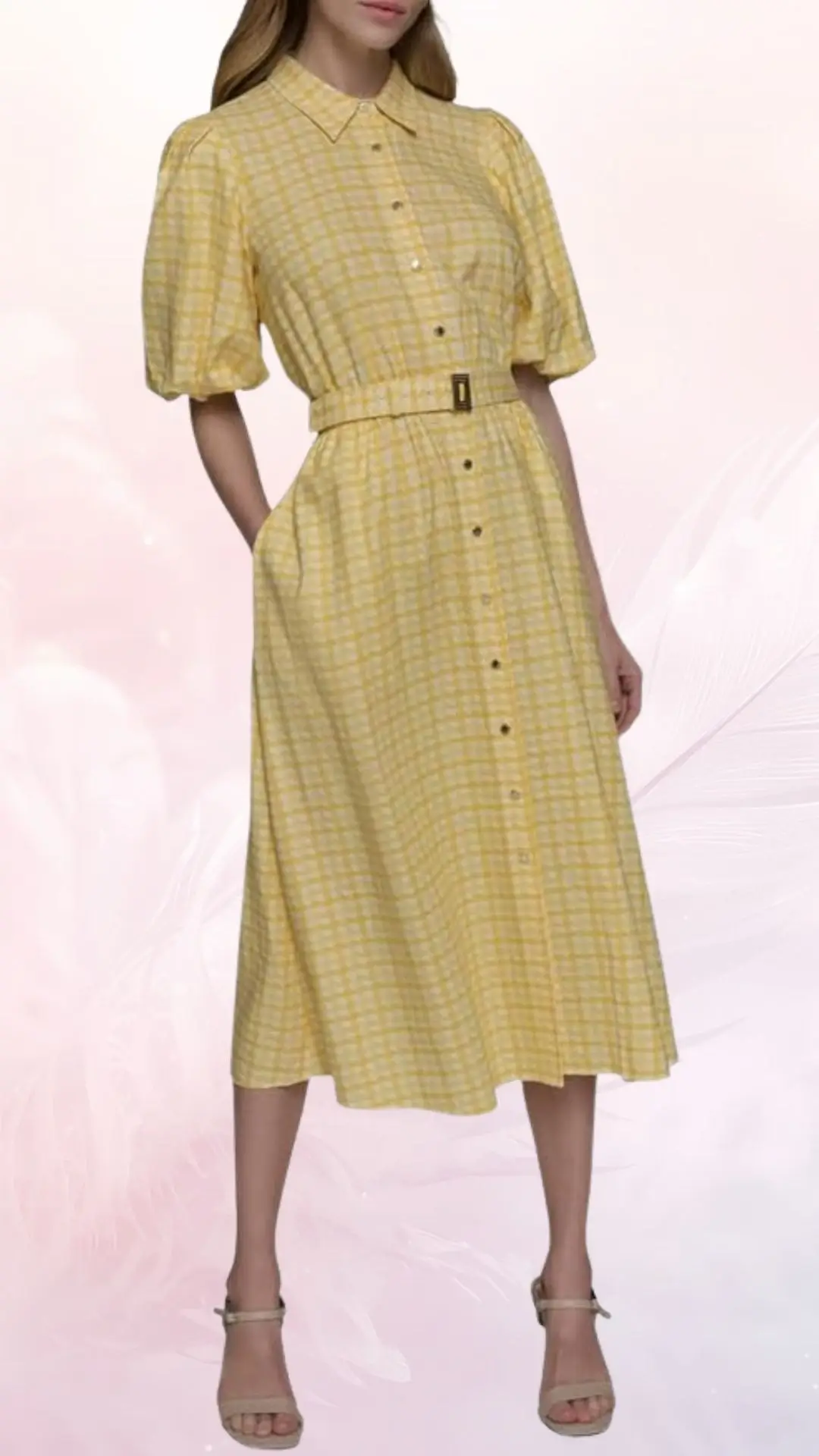 A lightweight, knee-length dress in a cheerful yellow and white check pattern features short puffed sleeves and a button-down front. The dress cinches at the waist with a belt, creating a flattering silhouette. It is styled with neutral-toned strappy heels, perfect for summer wedding celebrations.