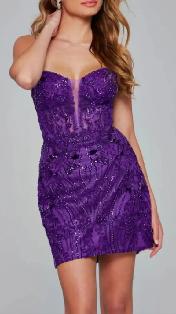 The dress features a vibrant shade of purple adorned with intricate beading and sequins, creating a shimmering effect. Its fitted bodice showcases a deep V-neckline and detailed patterns that flow outward, while the body-hugging silhouette transitions into a mini skirt with a subtle slit for added allure. This unique design beautifully balances sparkle with elegance, making it a standout choice for homecoming.