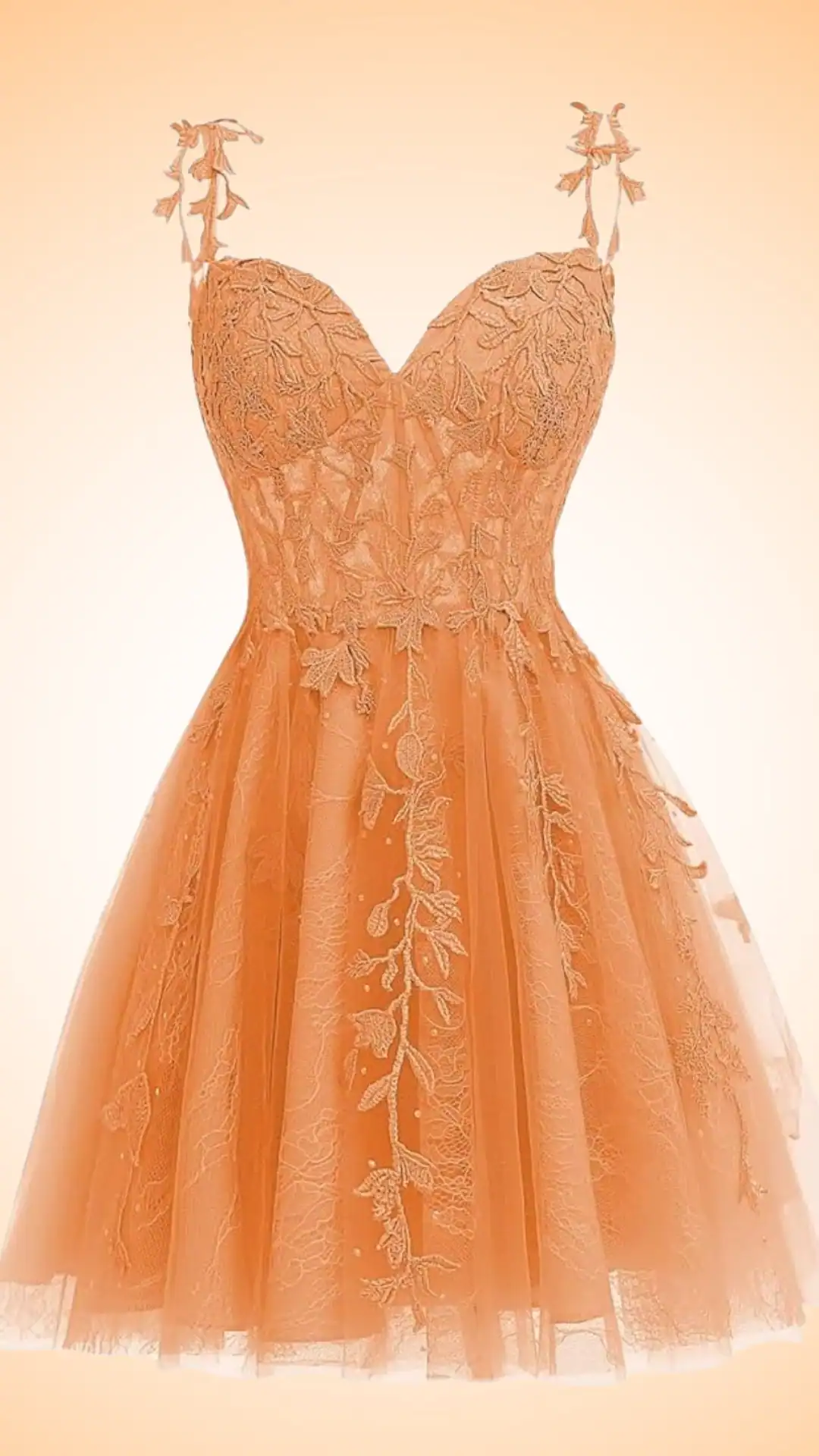 The dress features a fitted bodice with intricate floral lace overlay in a soft, peachy orange hue, complemented by delicate spaghetti straps adorned with floral accents. Its voluminous tulle skirt offers a playful and whimsical silhouette, perfect for a festive homecoming event, tailored for teenage girls seeking a romantic and trendy look.