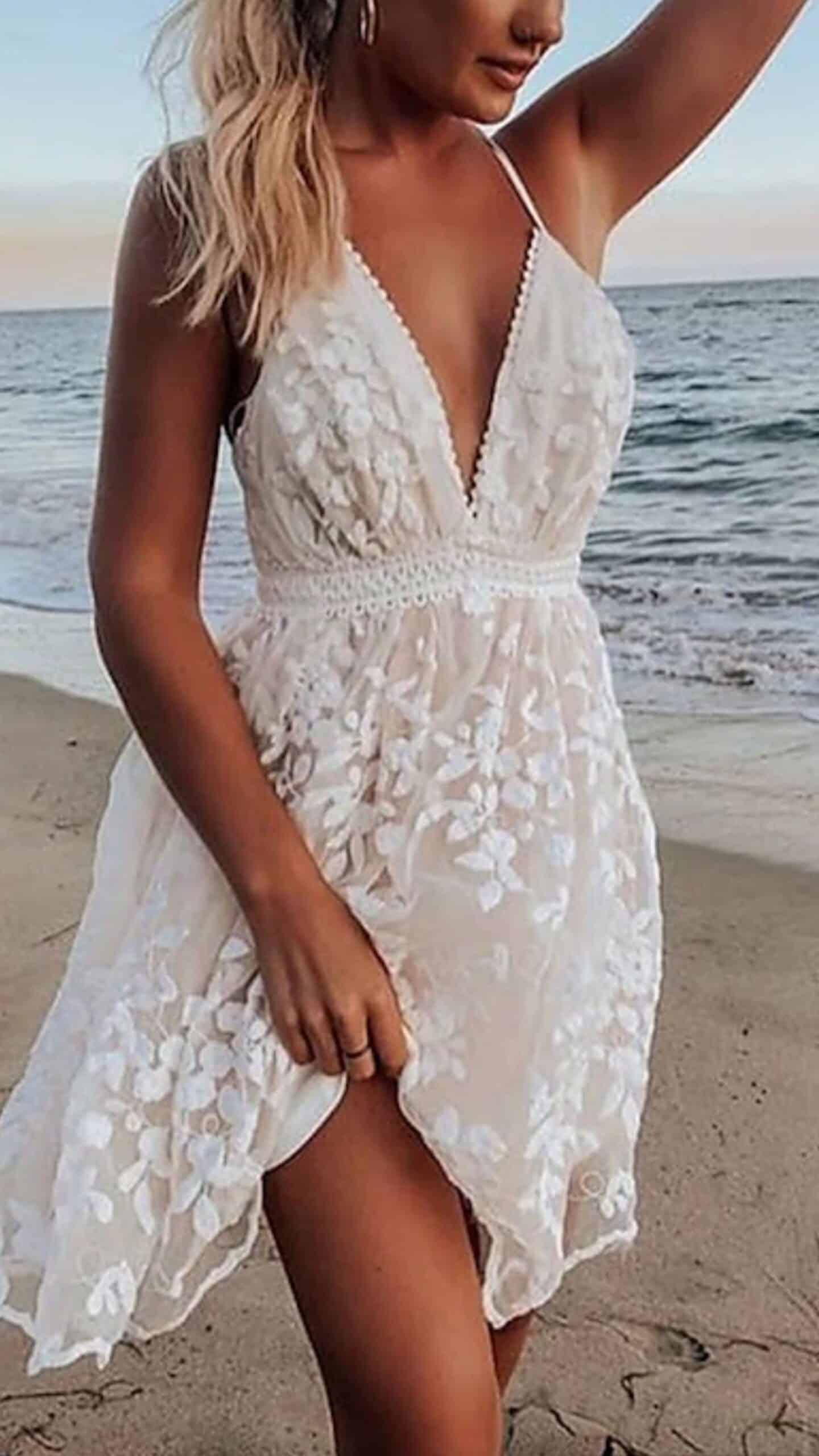 This white dress features a flowing A-line silhouette with a deep V-neckline and thin spaghetti straps, accentuating a feminine look. Made from a sheer, lightweight fabric adorned with floral embroidery, its high-low hemline adds a playful touch, making it perfect for a romantic beach wedding or summer outing.