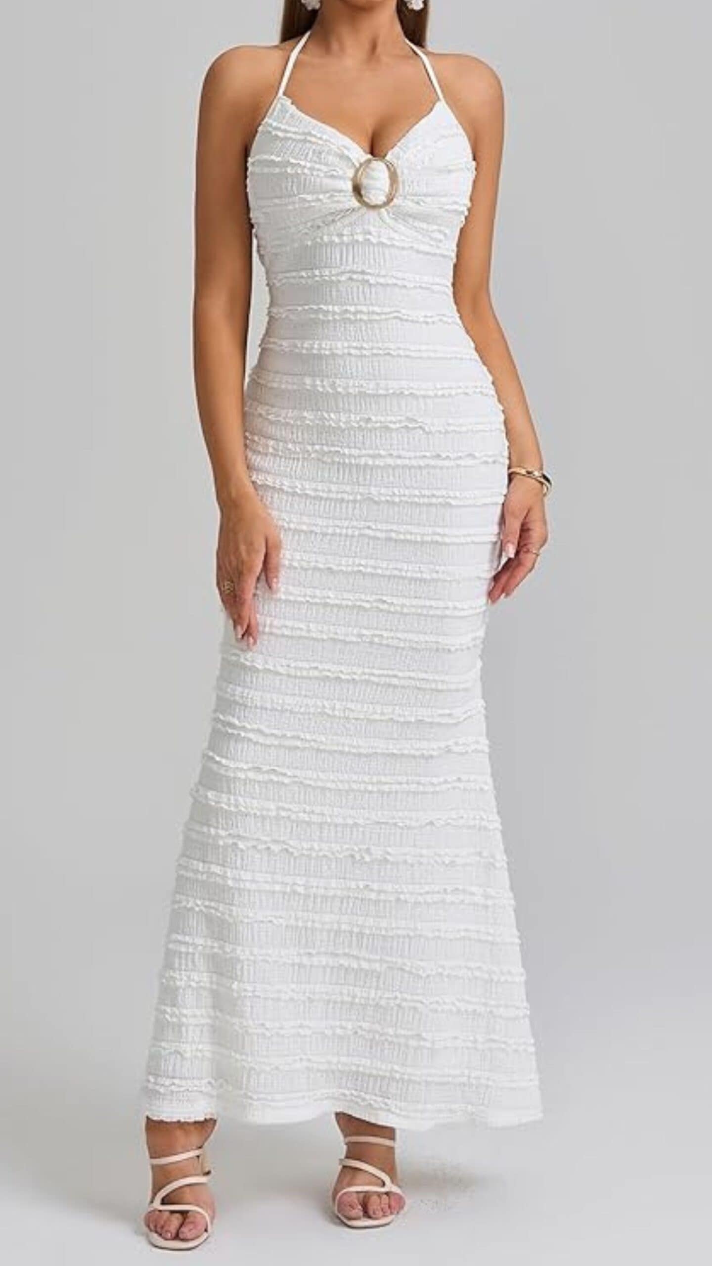 The dress features a fitted silhouette with a sweetheart neckline and halter straps, creating a flattering shape. Made from textured fabric with subtle ruched detailing, it is a crisp white color, extending to a full-length hem, ideal for formal events or weddings while exuding a romantic and elegant vibe.