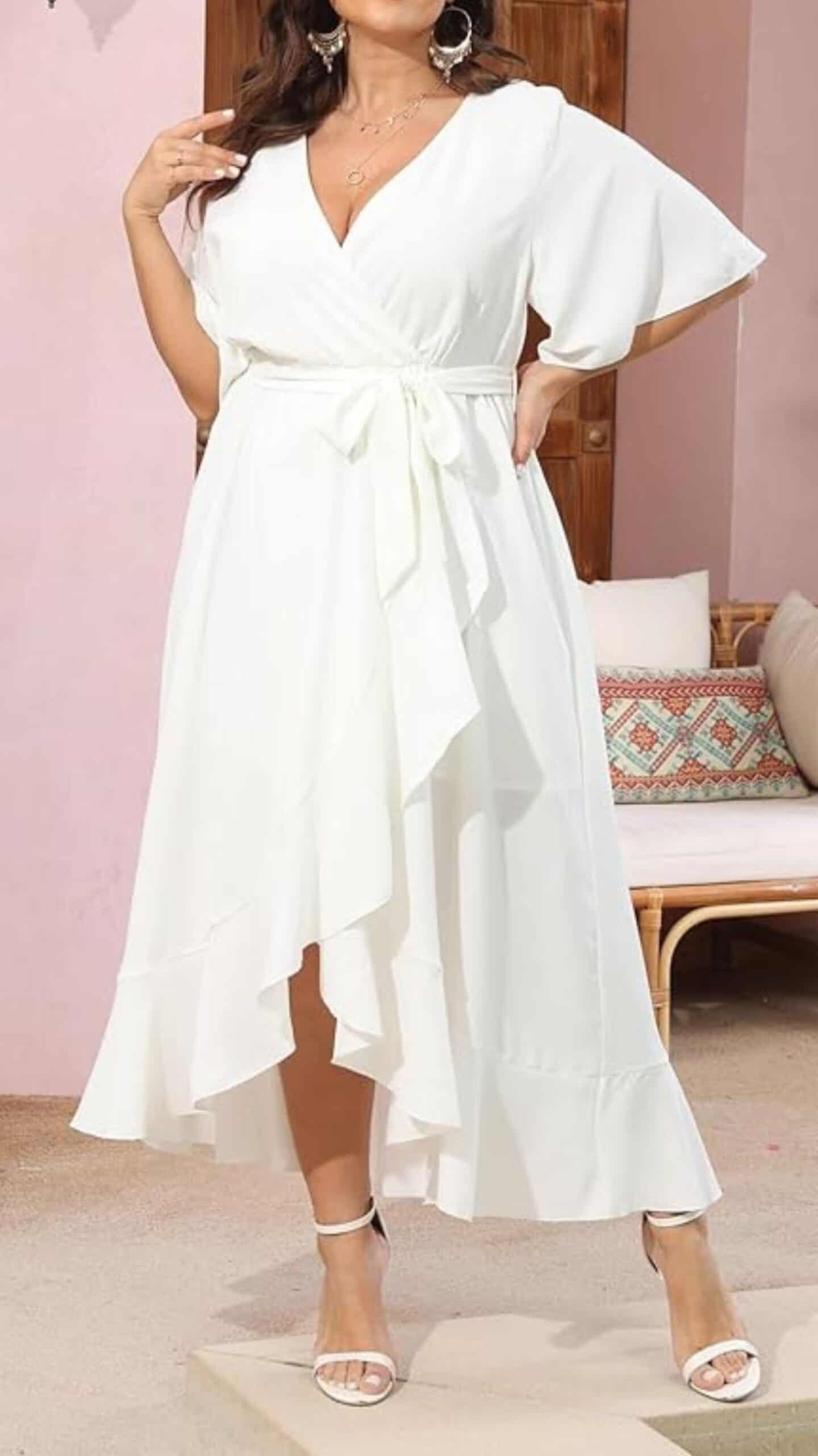A flowing, white wrap dress features a deep V-neckline and flutter sleeves, cinched at the waist with a fabric belt for a flattering silhouette. Crafted from a lightweight, textured fabric, it has a high-low hemline that adds movement and a romantic vibe, making it ideal for casual outings or summer events.