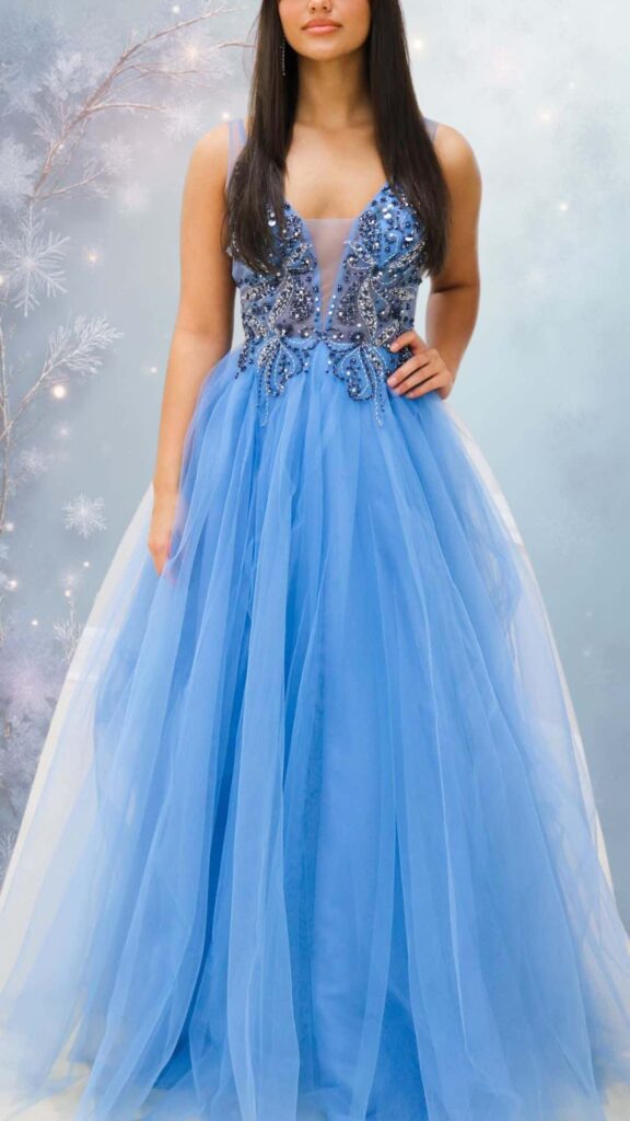 This elegant winter formal dress features a fitted bodice with a plunging neckline adorned with intricate silver beadwork, leading into a flowing, layered tulle skirt in a soft blue hue. The dress has thin straps and no sleeves, offering a chic silhouette while maintaining a lightweight feel, perfect for layering with a stylish coat. The combination of textures and embellishments adds a touch of glamour.