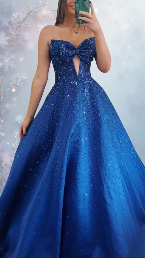 The dress features a stunning deep blue color with a strapless sweetheart neckline, adorned with a decorative bow at the center and a stylish cutout detail. The floor-length skirt showcases a smooth, satin texture, embellished with shimmering beadwork throughout, providing an elegant and chic aesthetic.