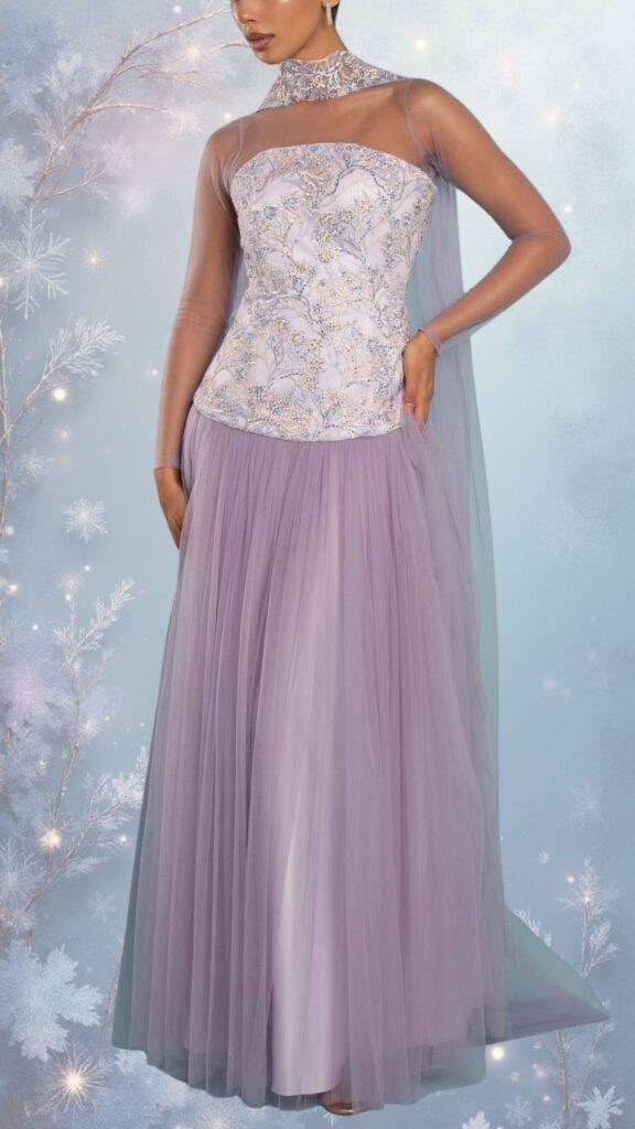 The dress features a fitted bodice with a high neckline and sheer long sleeves, crafted from intricately textured fabric adorned with delicate beadwork and floral patterns. The flowing skirt, made of soft tulle in a muted lavender hue, offers a graceful silhouette and added warmth, making it ideal for chilly. A cape-like overlay enhances the elegance while providing extra coverage.