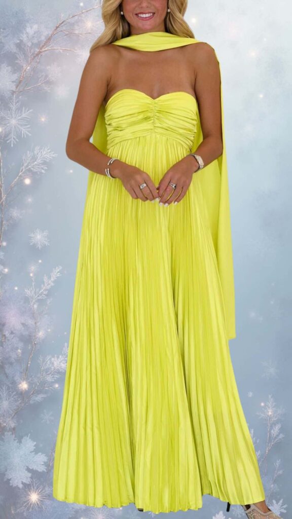 The dress features a strapless, sweetheart neckline with elegant pleating throughout, falling to a floor-length silhouette. Its vibrant yellow hue is complemented by a matching draped cape, adding sophistication while ensuring style in cooler weather. This design includes no slits or cutouts, making it a chic yet modest choice for fall and winter events.