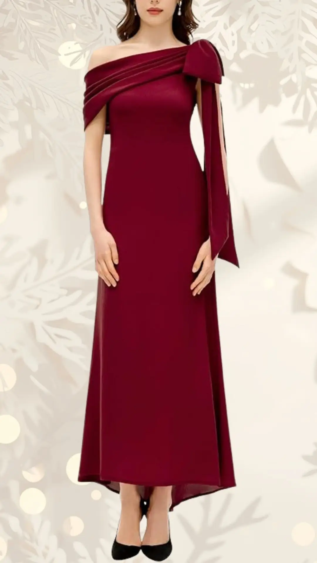 A burgundy off-shoulder wedding guest dress features a draped bodice and a large bow detail on one shoulder, adding elegance to its streamlined silhouette. The floor-length skirt flows gracefully, complemented by black heels. The background is softly patterned, enhancing the dress's rich color.