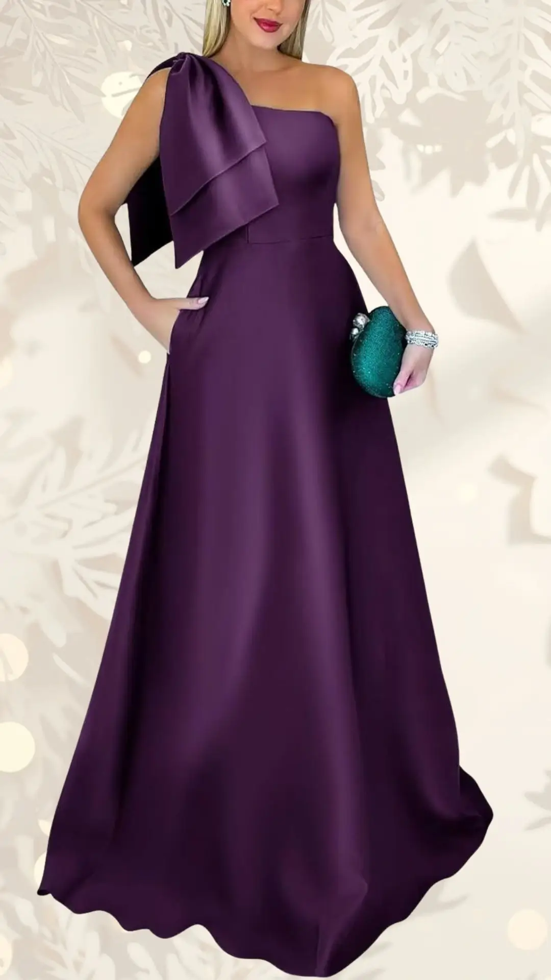 A rich purple wedding guest dress features a single strap with a dramatic bow detail on the shoulder. The floor-length gown has a fitted bodice and flows gracefully into a full skirt, complemented by a stylish green clutch held in the model's hand. Elegant yet modern, this dress combines simplicity with standout design elements.