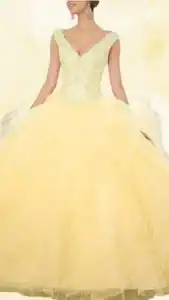 This yellow quinceañera dress features a deep V-neckline with delicate lace and beaded detailing on the bodice, providing a fitted look. The skirt is full and layered, made from soft tulle that flows elegantly to the floor with ruffled edges. The playful shade of yellow enhances its celebratory theme, making it perfect for a festive occasion.