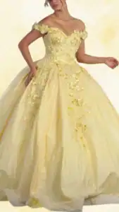 The dress features a vibrant yellow hue, with a sweetheart neckline and elegant off-the-shoulder sleeves. Its voluminous ball gown silhouette is adorned with intricate floral appliqués and sparkling embellishments cascading down the skirt, creating a soft, romantic look. The hemline is finished with a subtle shimmer, enhancing the overall luxurious feel of the dress.