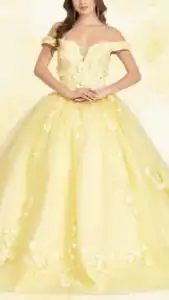 This yellow quinceañera dress features an off-the-shoulder neckline and a fitted bodice adorned with intricate floral embroidery. The voluminous skirt flows to the floor, embellished with delicate white floral patterns that enhance its vibrant color. The overall look is elegant and celebratory, perfect for a special occasion.